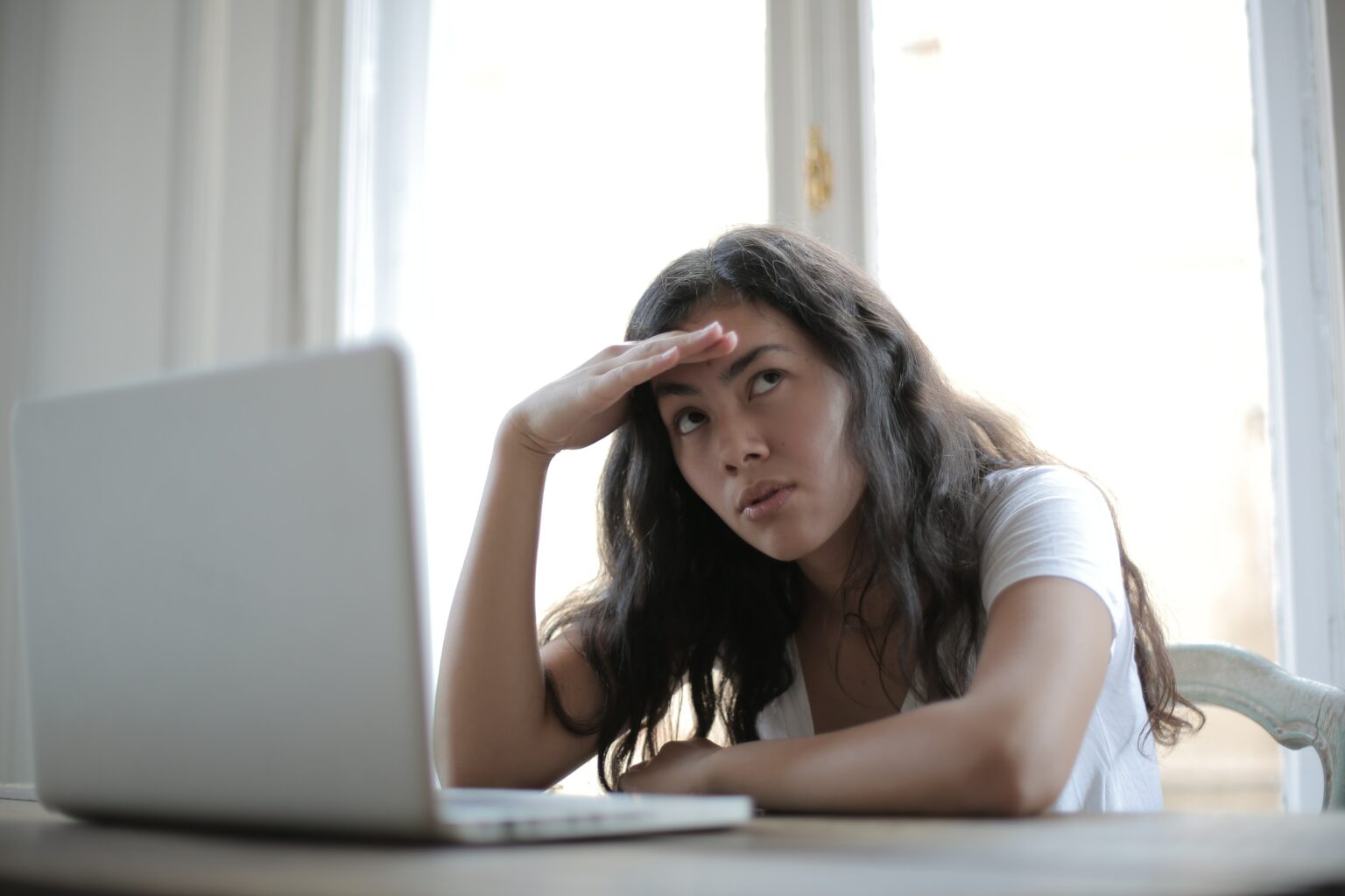 Woman sitting at laptop computer holding her head and rolling her eyes.