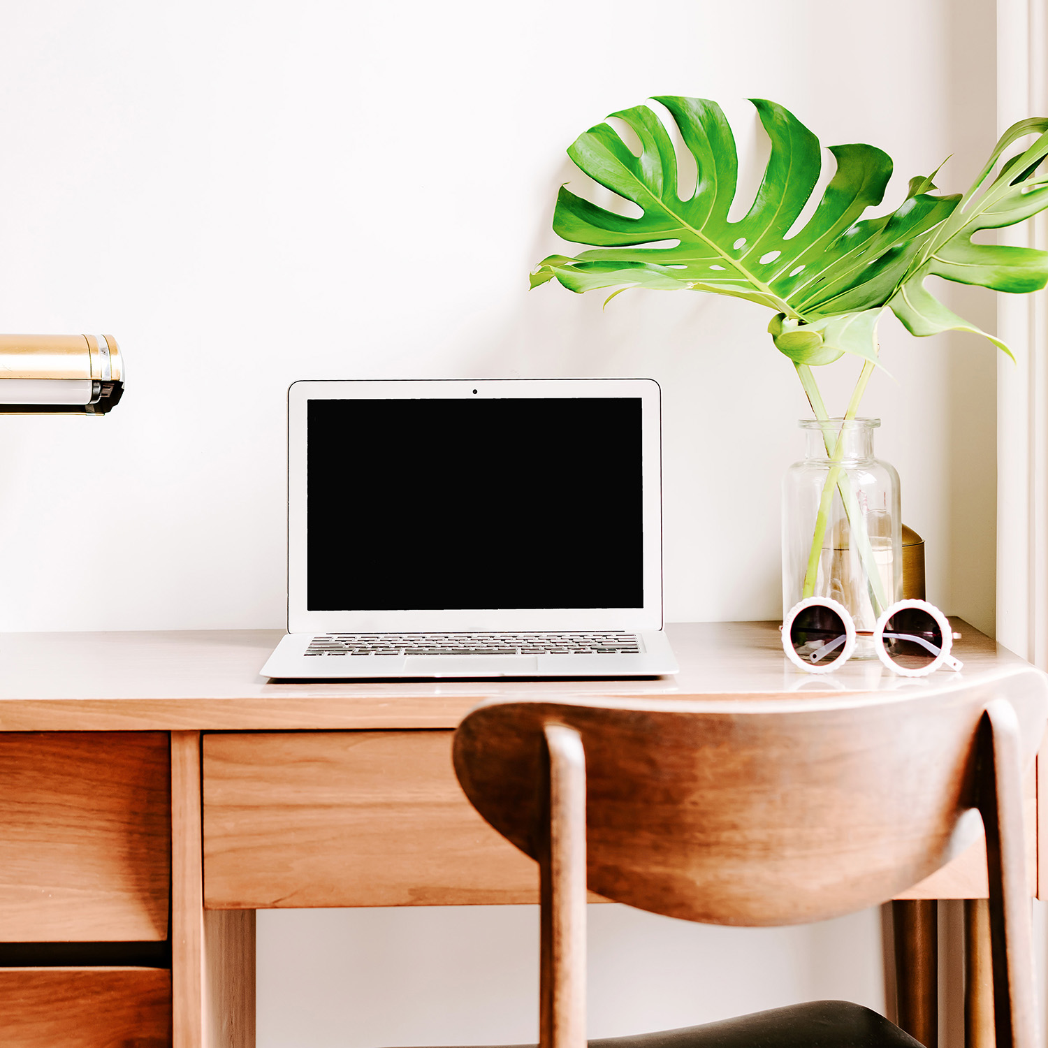 an open laptop on a desk with a plant and sunglasses