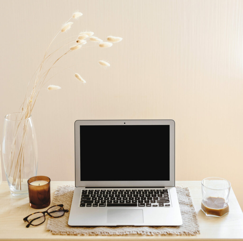 open laptop on desk with flowers, a candle, glasses and a cup of coffee